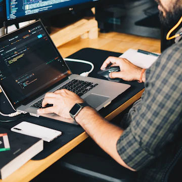 Developer writing code on a laptop next to a large monitor