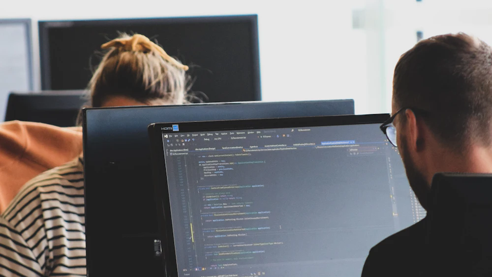 Two developers writing code at monitors in a bright workspace