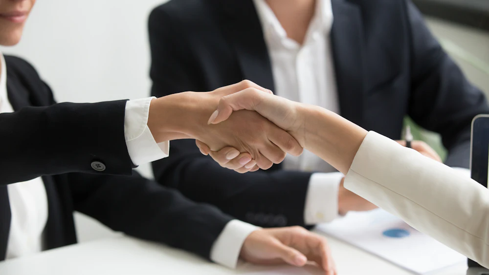 Two people shaking hands over a laptop after agreeing a plan